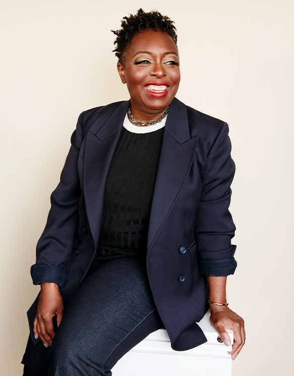 International Women's Day 2021: Kimberly Bryant Founder and CEO of Black Girls Code in a navy blazer, black sweater and jeans with a gemstone necklace and gold bracelet