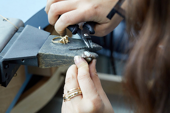 The RealReal x Catbird. Photograph of a female jeweller at a work bench, holding pliers and working on a piece from the sustainable fine jewelry upcycled collection