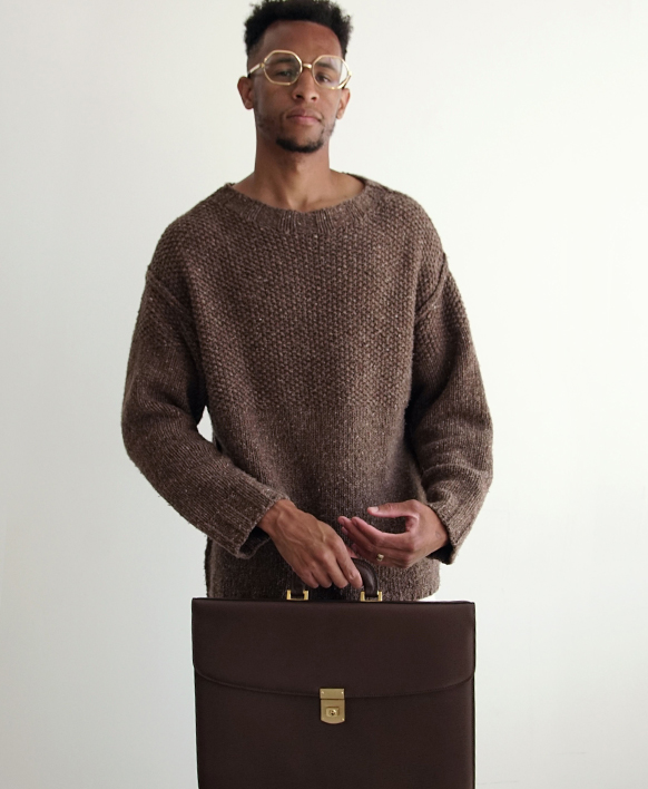 Caleb wearing a brown sweater and brown Mark Cross men's bag