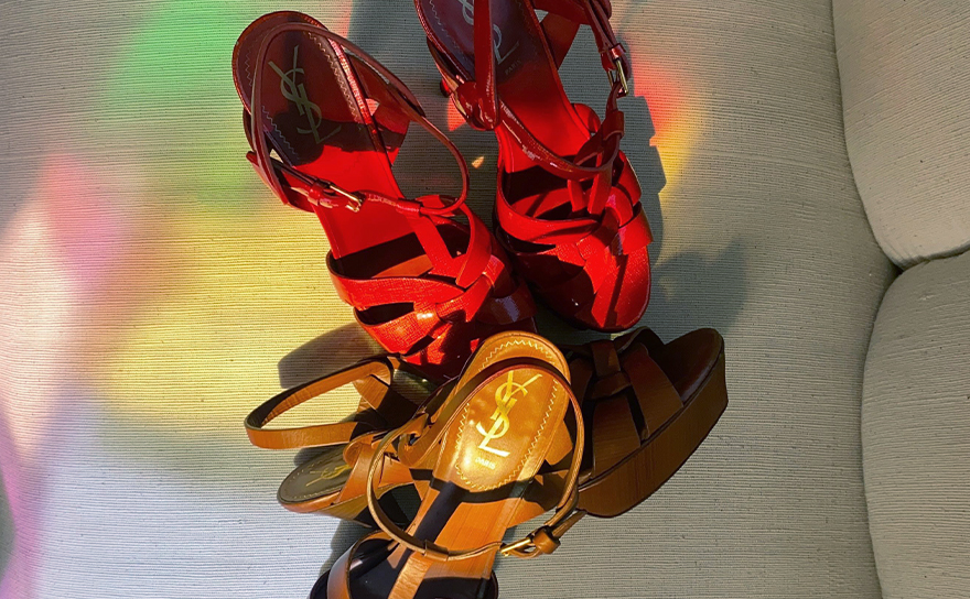 Red and brown YSL Tribute sandals on a white couch with rainbow light